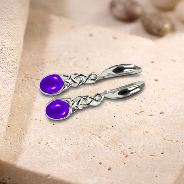 Boucles d'oreilles en améthyste violette, cabochon ovale et nœud celtique en argent 925 rhodié, posées sur du travertin