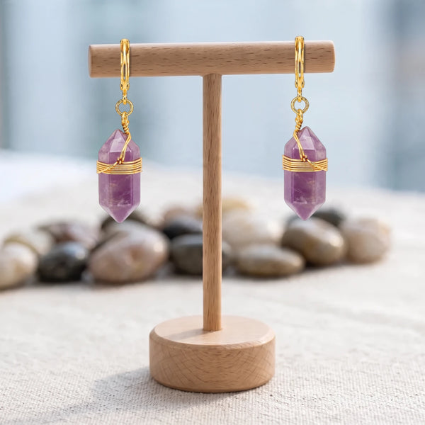 Boucles d'oreilles pierre violette, pointe d'améthyste sertie de fil doré sur créole, suspendues à un présentoir en bois