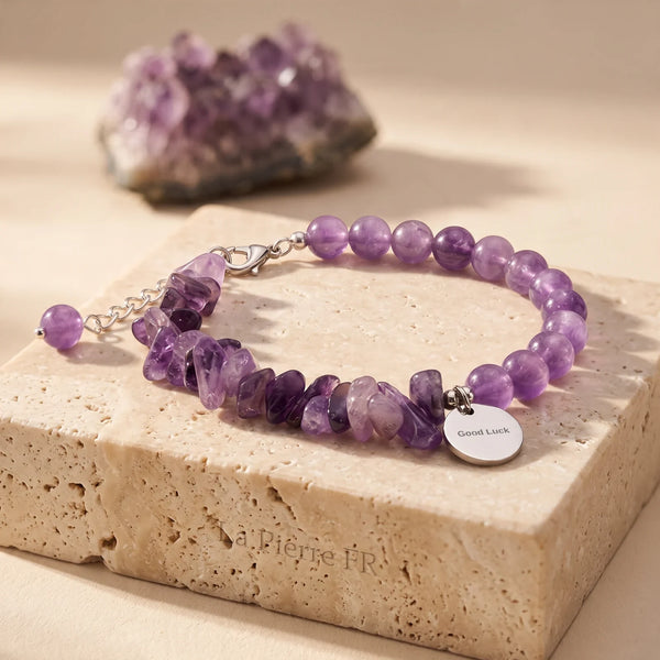 Bracelet améthyste DUO®, pierre baroque et perles rondes violettes sur chaîne argentée, posé sur travertin