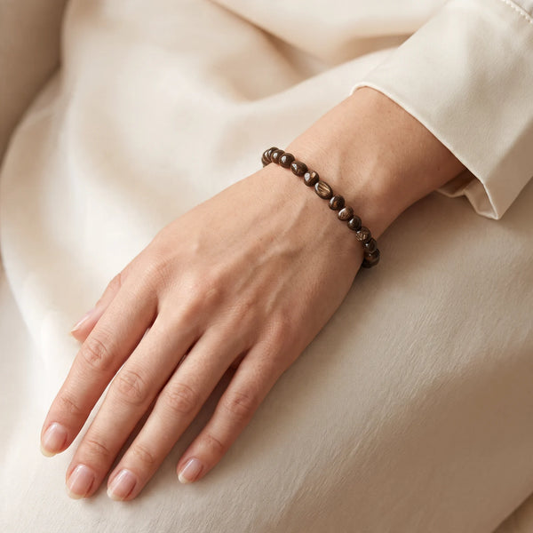 Bracelet bronzite porté au poignet d'une femme, pierres roulées brun chocolat chatoyantes