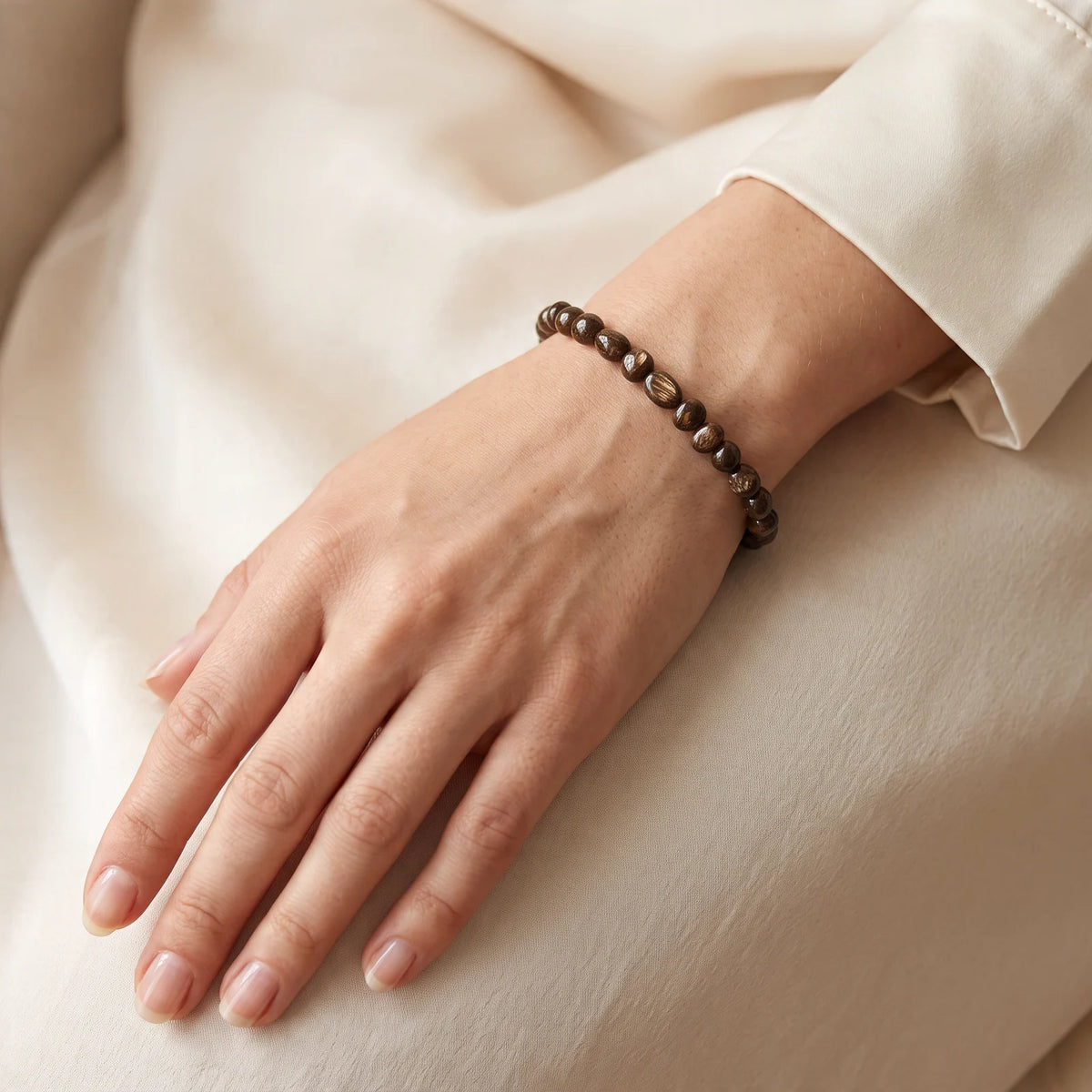 Bracelet bronzite porté au poignet d'une femme, pierres roulées brun chocolat chatoyantes