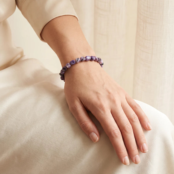 Bracelet charoïte porté au poignet d'une femme, pierres roulées mauves veinées de noir