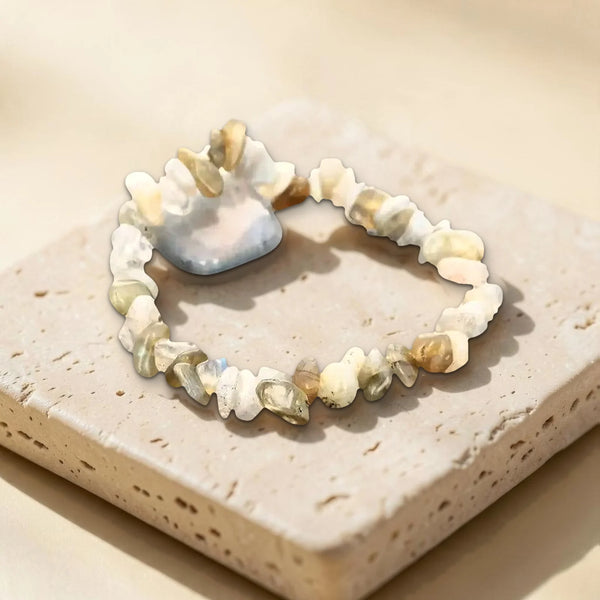 Vraie photo du bracelet labradorite et de sa pierre roulée grise posés sur du travertin