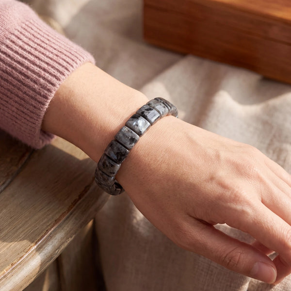 Bracelet larvikite au poignet d'une femme, plaques grises aux éclats bleu argenté