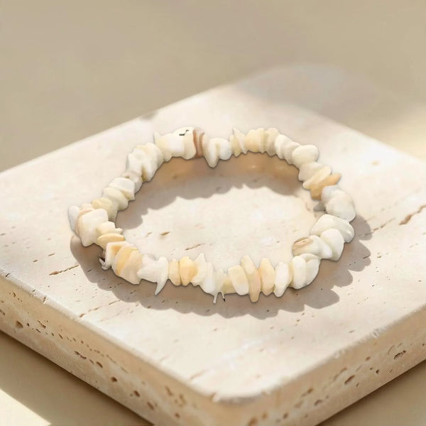 Bracelet élastique en pépites de nacre naturelle aux reflets ivoire, posé sur un bloc de travertin