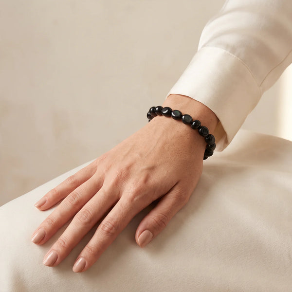 Bracelet obsidienne arc-en-ciel porté au poignet d'une femme, pierres roulées noires