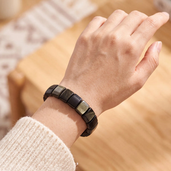 Bracelet en obsidienne dorée au poignet d'une femme, plaques noires au halo doré