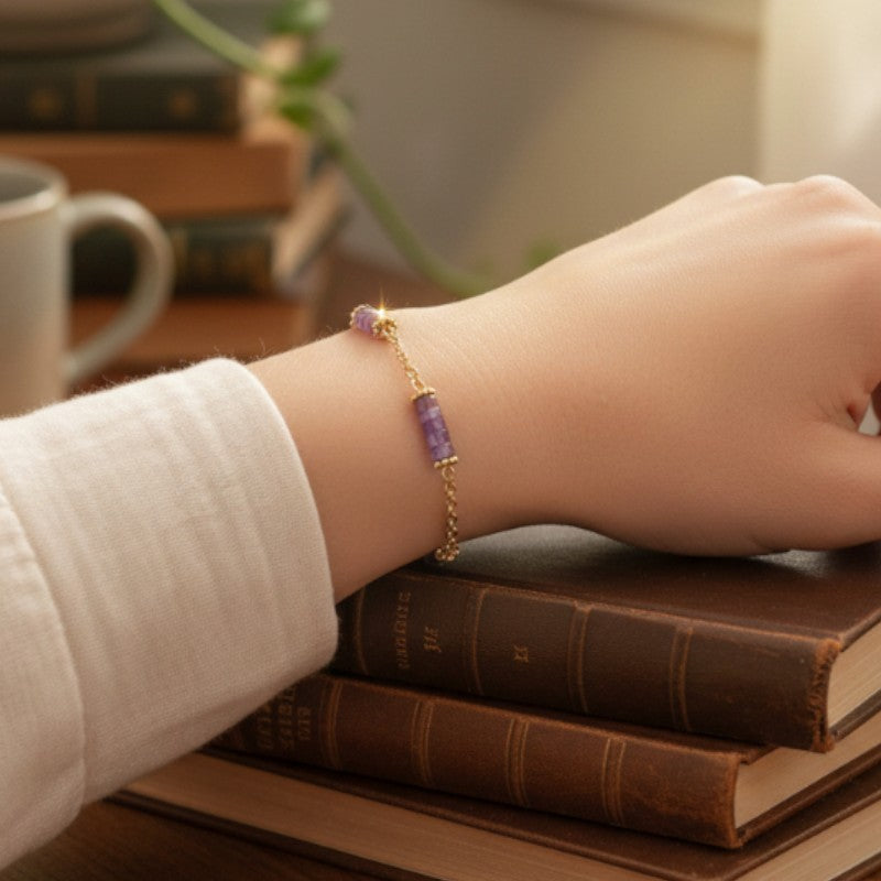 Bracelet heishi en améthyste porté au poignet d'une femme, perles violettes et chaînette dorée QUATUOR®