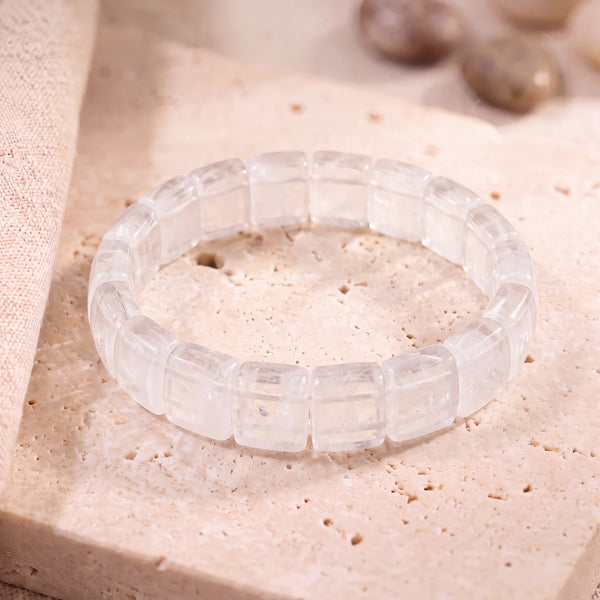 Bracelet cristal de roche en plaques plates de 14 mm, pierre transparente polie, posé sur une dalle de travertin