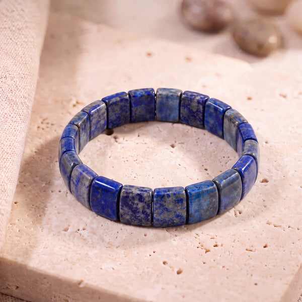 Bracelet lapis lazuli en plaques de 14 mm, pierre bleue à paillettes dorées, posé sur une dalle de travertin