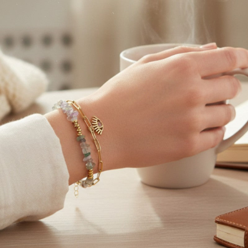 Bracelet mauvais œil en fluorine porté au poignet d'une femme, pierres violettes et vertes et chaîne dorée OCULUS®