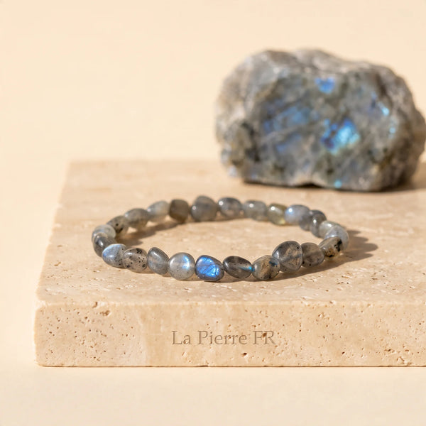 Bracelet en labradorite roulée grise aux reflets bleus, idée cadeau en pierre naturelle posé sur travertin
