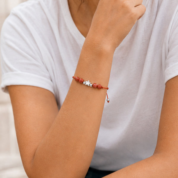 Bracelet pierre naturelle jaspe rouge porté au poignet d'une femme, cordon rouge et étoile argentée ÉTOILE®
