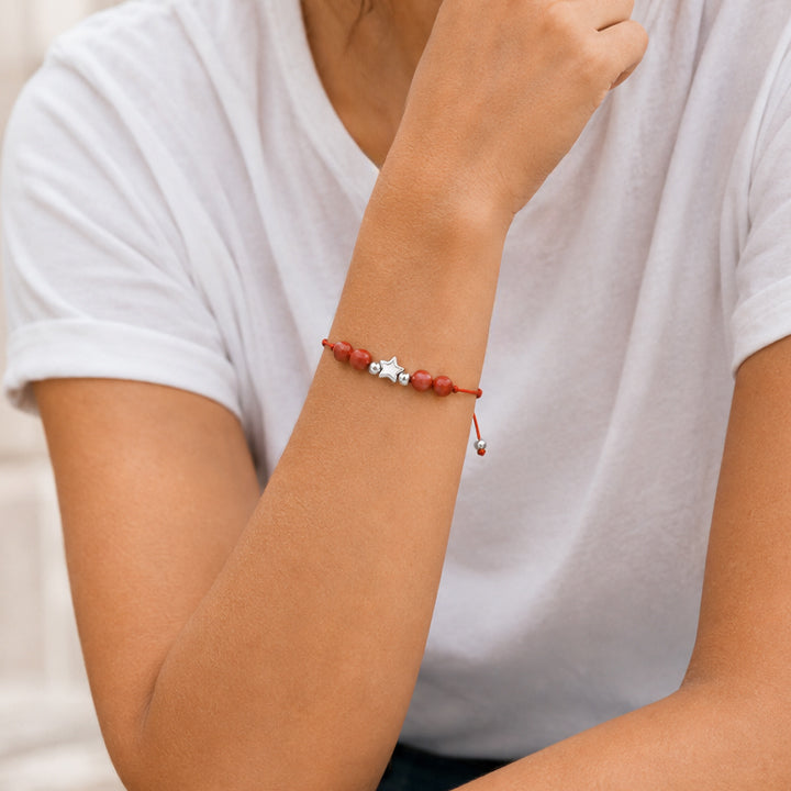 Bracelet pierre naturelle jaspe rouge porté au poignet d'une femme, cordon rouge et étoile argentée ÉTOILE®