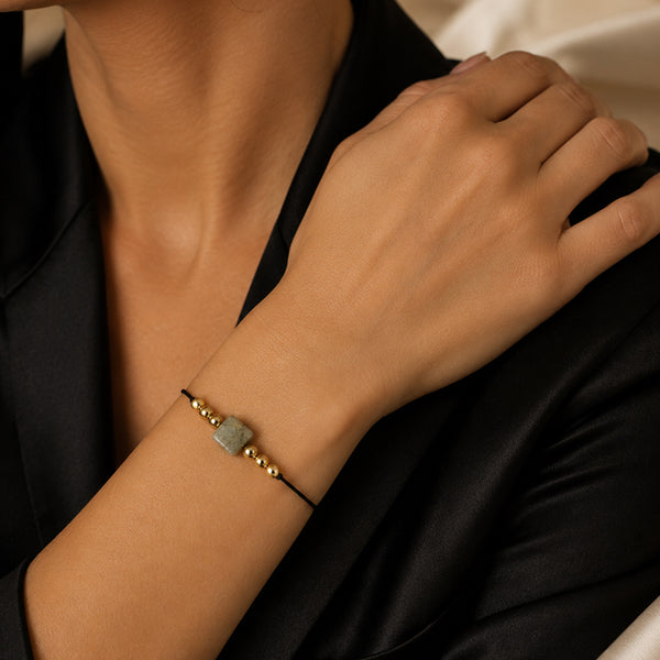 Bracelet pierre naturelle labradorite porté au poignet d'une femme, cube gris à reflets bleus et cordon doré CUBE®