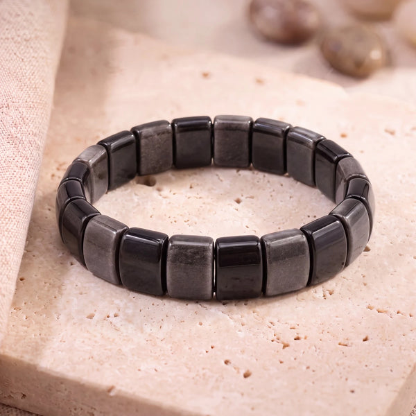 Bracelet obsidienne argentée en plaques plates de 14 mm, pierre noire à reflet argenté, sur une dalle de travertin