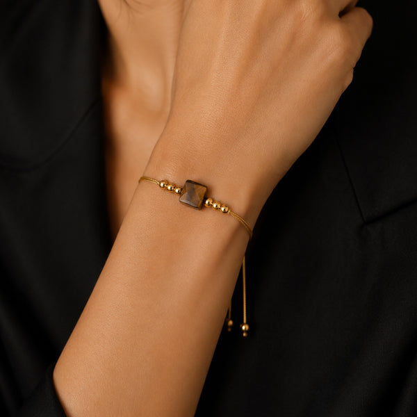 Bracelet pierre naturelle œil de tigre porté au poignet d'une femme, cube miel et cordon doré CUBE®