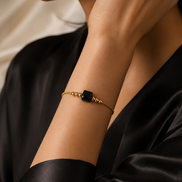 Bracelet pierre naturelle onyx noir porté au poignet d'une femme, cube noir et cordon doré CUBE®