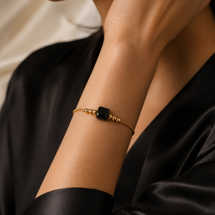 Bracelet pierre naturelle onyx noir porté au poignet d'une femme, cube noir et cordon doré CUBE®