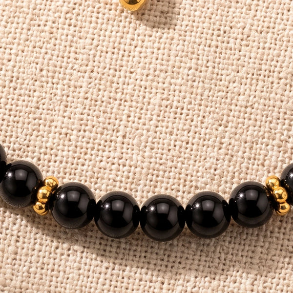 Gros plan sur les perles d'onyx noir de 4 mm et les rondelles fleurs dorées du bracelet ORÉLIA®