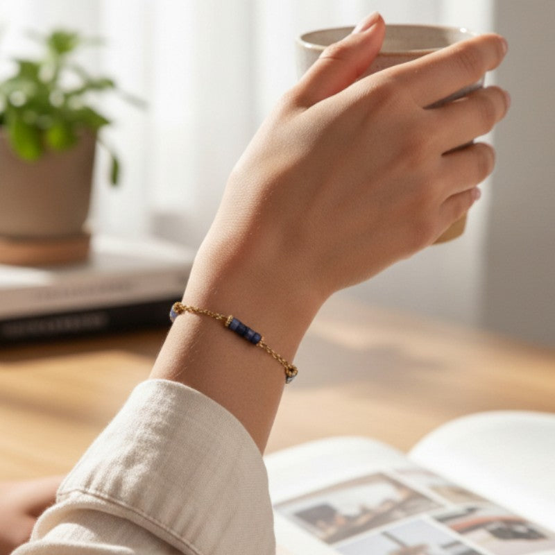 Bracelet heishi en sodalite porté au poignet d'une femme, perles bleues et chaînette dorée QUATUOR®
