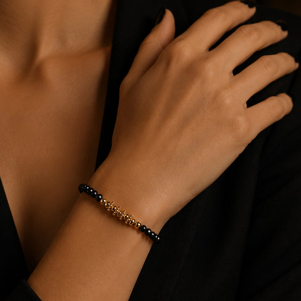 Bracelet pierre spinelle noir FINA® porté au poignet d'une femme, perles facettées et perles dorées