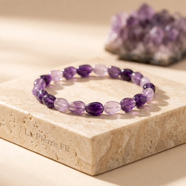Bracelet améthyste en pierres roulées violettes posé sur un bloc de travertin, idée cadeau en pierre naturelle