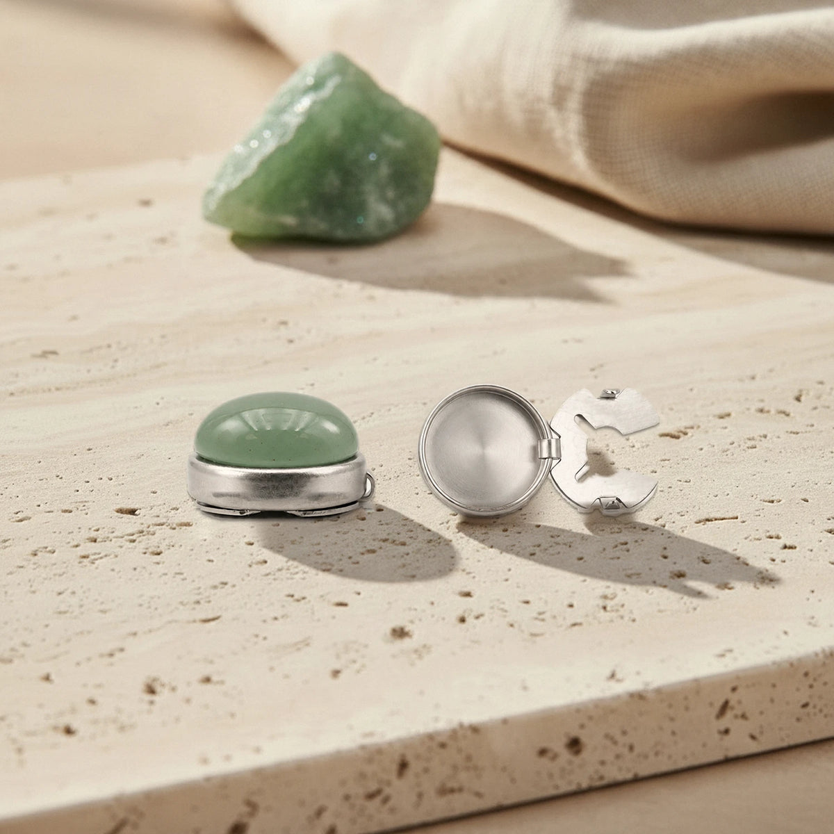 Cache bouton en aventurine verte avec son clip en acier inoxydable ouvert, posé sur du travertin