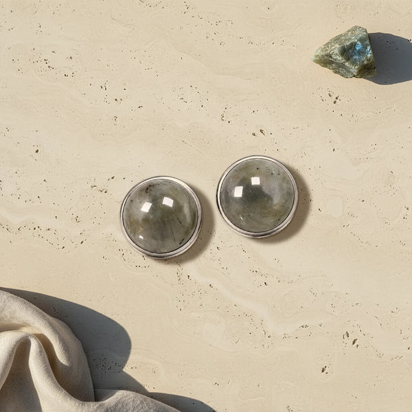 Cache bouton gris en labradorite naturelle, deux cabochons sertis d'acier posés à plat sur du travertin