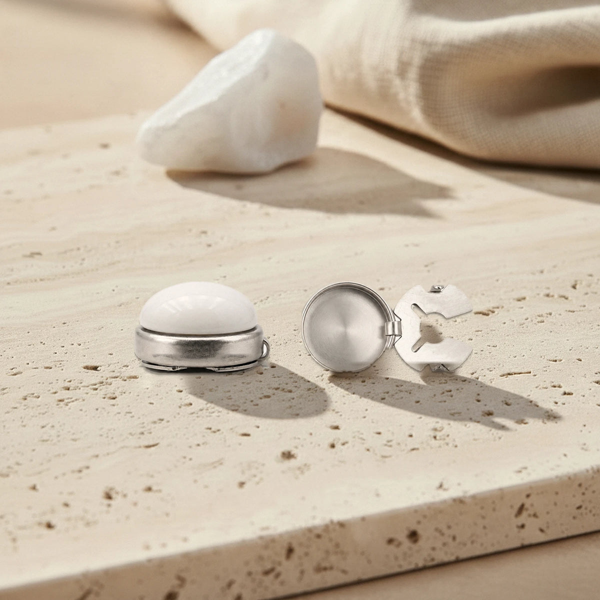 Cache bouton en jade blanc à clipser, cabochon serti et fermoir à clip en acier inoxydable, posés sur du travertin