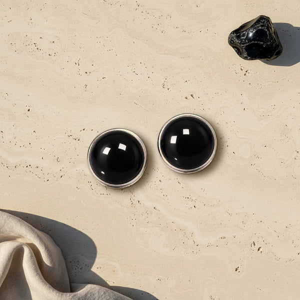 Cache bouton noir en obsidienne noire brillante, deux cabochons sertis d'acier posés à plat sur du travertin