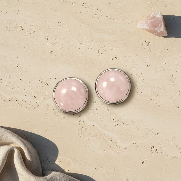 Cache bouton rose en quartz rose naturel, deux cabochons sertis d'acier posés à plat sur du travertin