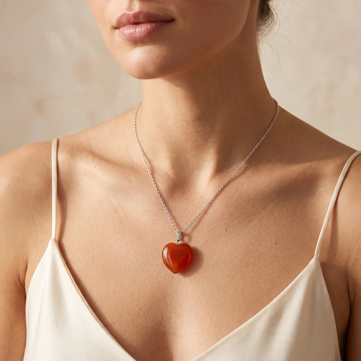 Collier pendentif cœur en cornaline orange porté par une femme, chaîne argentée