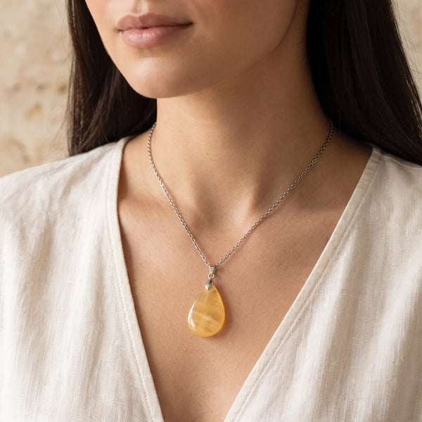 Collier pendentif goutte en calcite orange naturelle porté par une femme, chaîne argentée