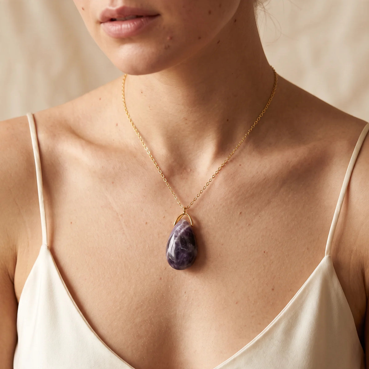Collier pendentif larme en améthyste rubanée naturelle porté par une femme, chaîne dorée