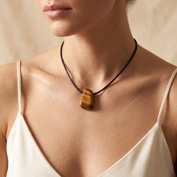 Collier pendentif pierre roulée percée en œil de tigre naturel porté par une femme, cordon noir