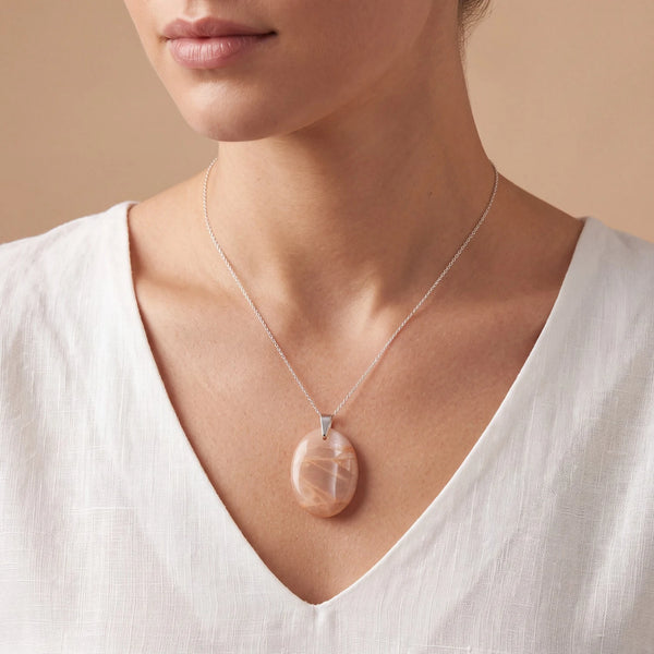 Bijou pierre de lune orange porté par une femme, pendentif ovale plat couleur abricot