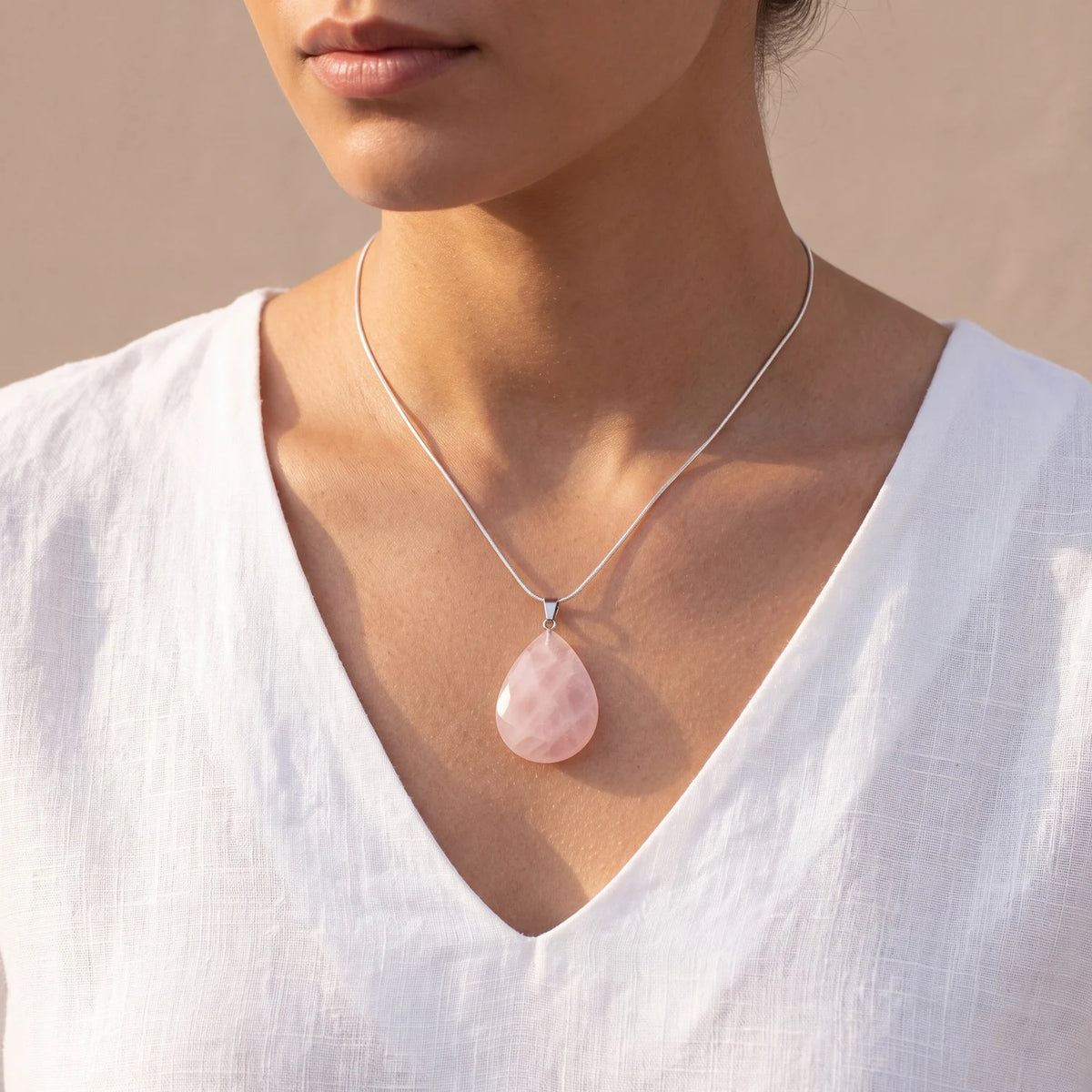 Pendentif quartz rose de lithothérapie porté par une femme, goutte plate rose tendre