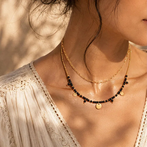 Collier superposé en onyx noir porté par une femme, chaîne et perles dorées