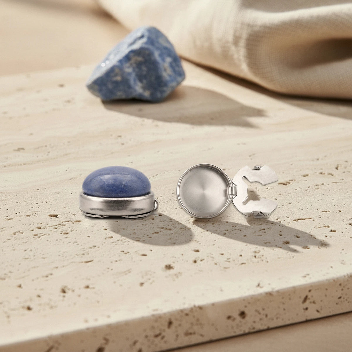 Couvre bouton de chemise en aventurine bleue, un fermé et un ouvert montrant la coupelle et le clip en acier, sur travertin