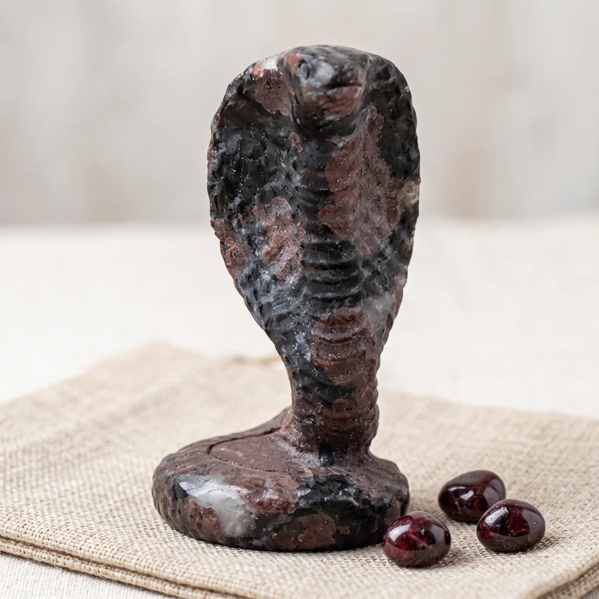 Figurine cobra en pierre naturelle sur un lin avec trois pierres roulées de grenat rouge