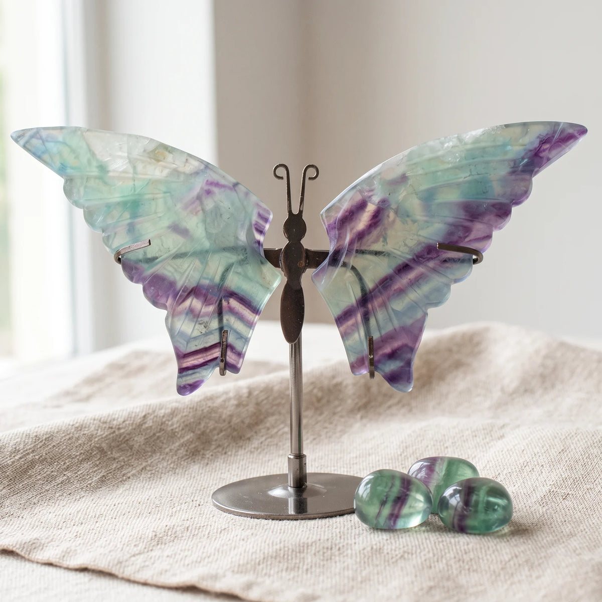 Figurine papillon en fluorine sur un lin naturel avec trois pierres roulées