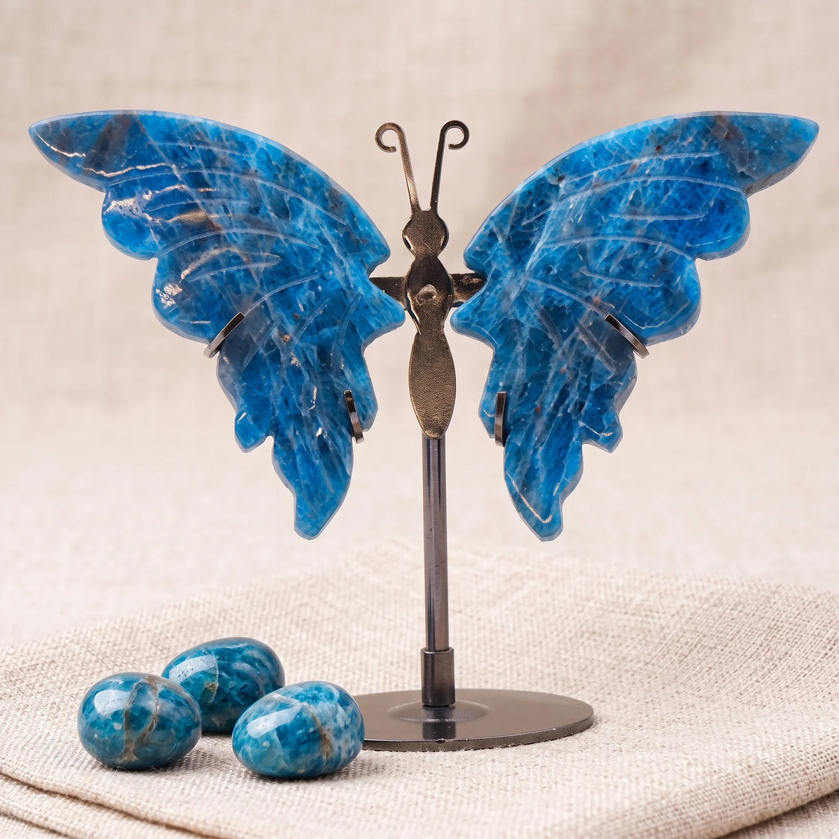 Figurine papillon en pierre naturelle apatite bleue sur un lin naturel avec trois pierres roulées