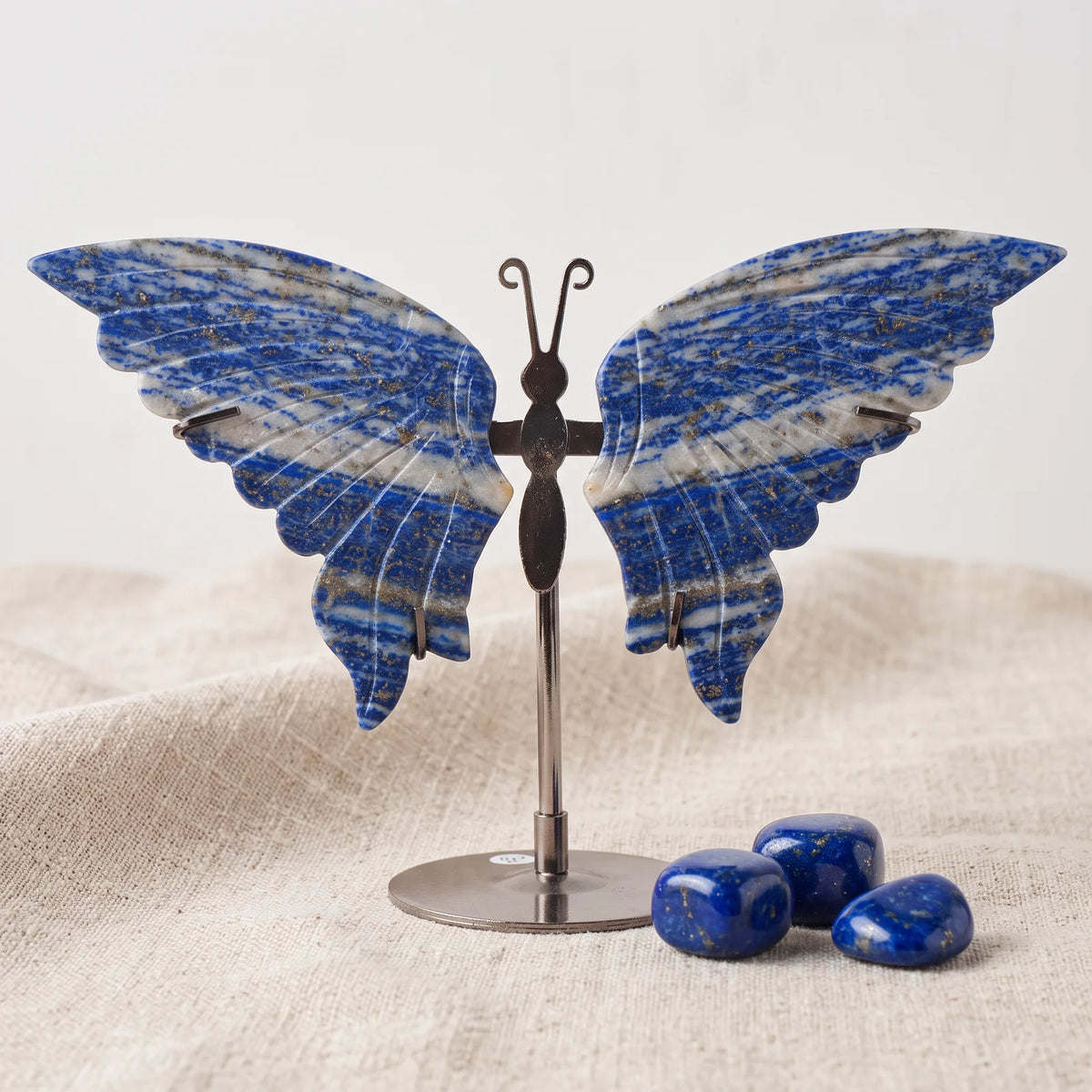 Figurine papillon en pierre bleue lapis lazuli sur un lin naturel avec trois pierres roulées