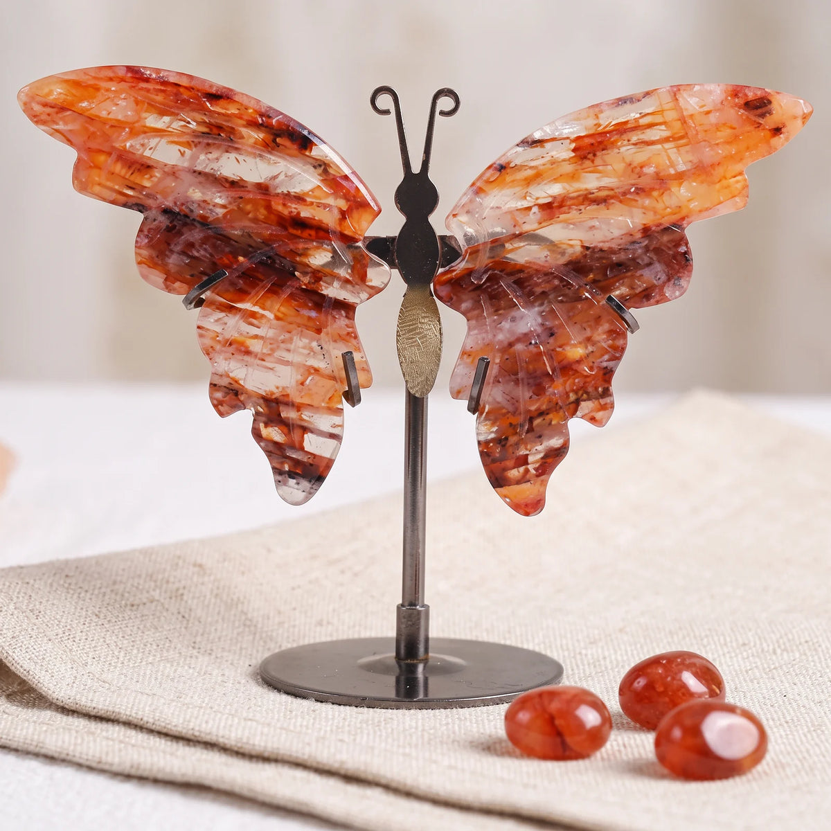 Figurine papillon en quartz hématoïde du Brésil sur un lin naturel avec trois pierres roulées