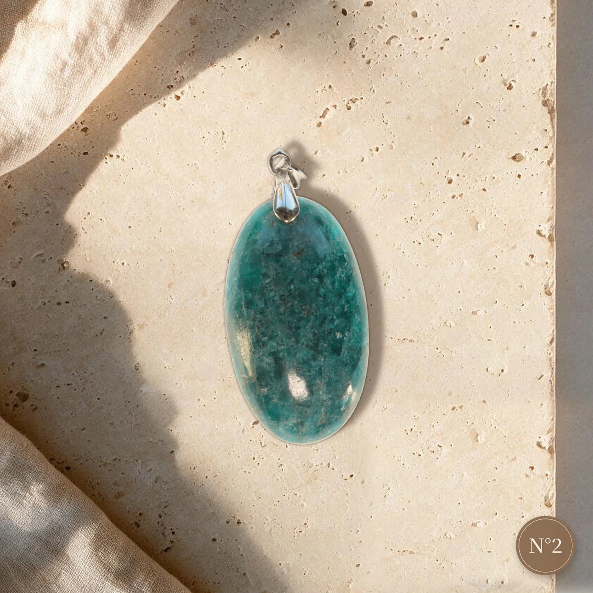 Pendentif apatite bleue pièce unique N°2, ovale allongé bleu vert profond et bélière argentée sur travertin