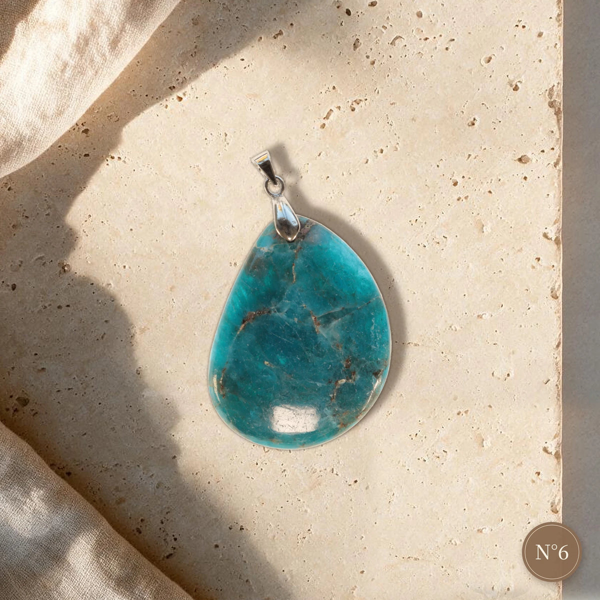 Pendentif apatite bleue pièce unique N°6, goutte bleu lagon veinée de brun et bélière argentée sur travertin