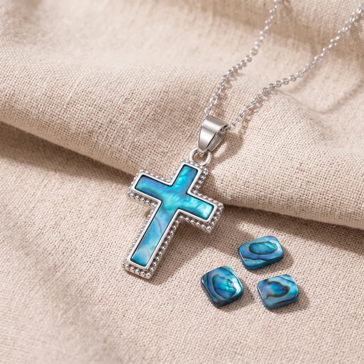 Pendentif croix dentelée en nacre d'ormeau bleue sur un lin naturel avec des éclats de nacre