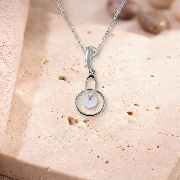 Pendentif pierre de lune véritable, modèle rond au centre d'un anneau d'argent, sur une dalle de travertin
