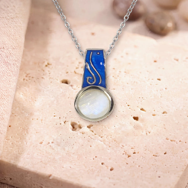 Collier pendentif pierre de lune, modèle rond à bélière émaillée, sur sa chaîne, posé sur une dalle de travertin
